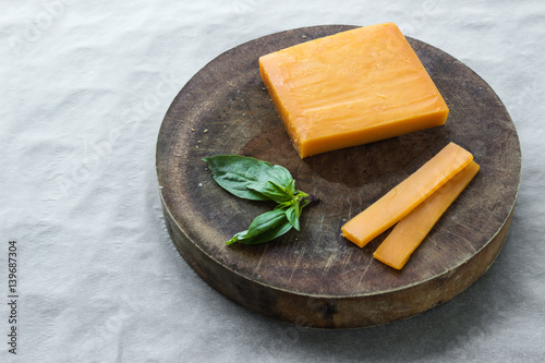 Block cheddar cheese, slices and basil leaves on cutting board