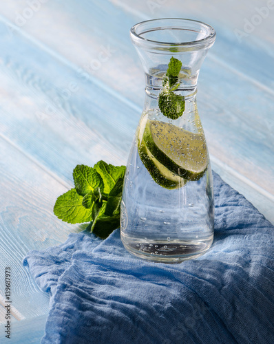 Bottle with water, slices of lime and leafs of mint on blue woodden background photo