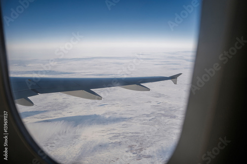 View from aircraft window as frame at wing of airliner and clouds beneath
