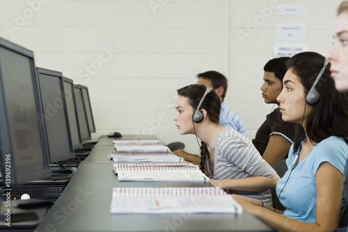 Students studying in computer lab, one leaning forward to see screen