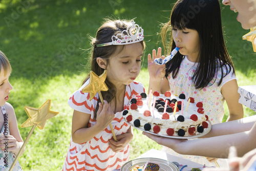 Girl blowing out candles on birthday cake at outdoor birthday party photo