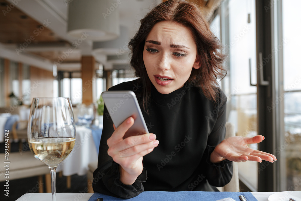 Displeased Woman in restaurant looking at phone Displeased Woman in restaurant looking at phone