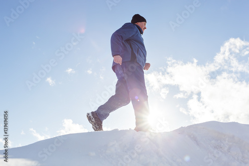 An elderly man running in the winter. Jogging across the snow on a sunny day