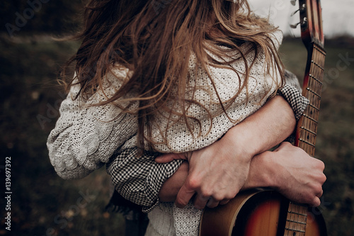 Photo man with guitar hugging his boho gypsy woman closeup in windy field