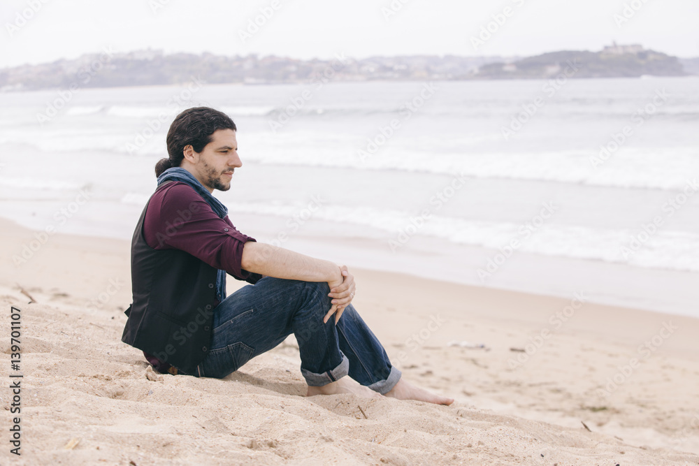 caucasian hipster man sitting on the sand with casual clothes caucasian hipster man sitting on the sand with casual clothes