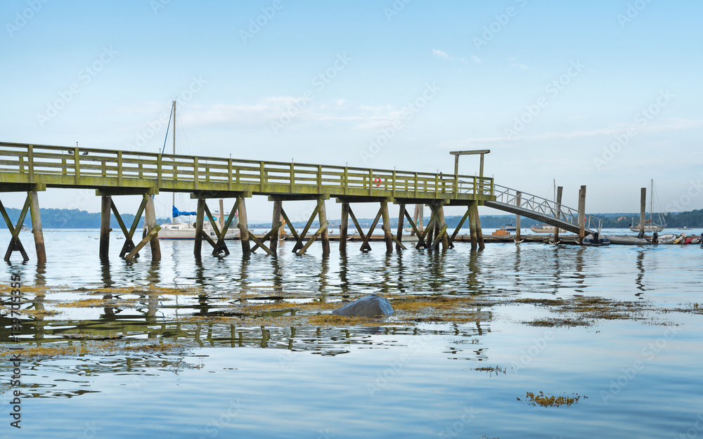 Very long pier extending over the water with sailboats in distance at Stockton Springs, Maine.