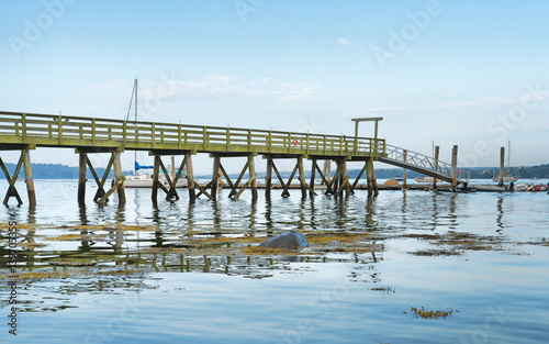 Very long pier extending over the water with sailboats in distance at Stockton Springs, Maine. © Bert Folsom