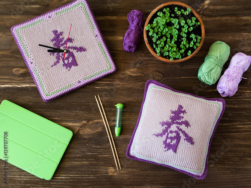 Knitted handmade watches, square pillow, needles and lilac, green, white yarn balls on wooden table. Translation of the hieroglyph is SPRING.