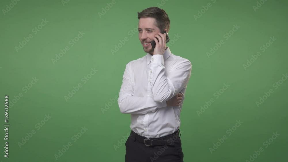 Young handsome man in white shirt standing, talking on the phone and smiling, chroma key green screen background Young handsome man in white shirt standing, talking on the phone and smiling, chroma key green screen background