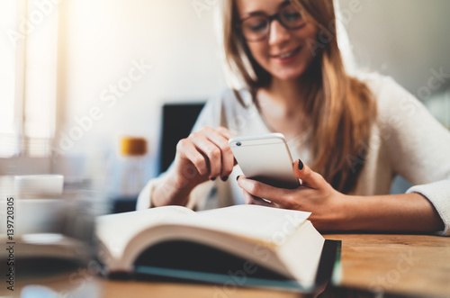 Happy smiling young girl using smartphone while working at modern coworking space, hipster girl with long hair chatting with friends at social networks, female freelancer working at home