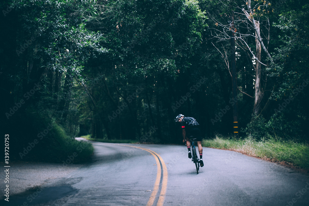 A fashionable cyclist rides his bikes on a dark road covered by forest and jungle