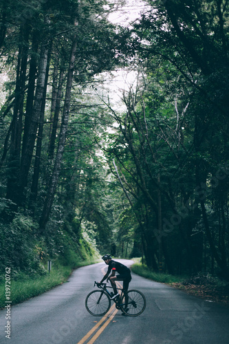 A silhouette of a cyclist standing in the middle of the road in santa cruz, covered by dark forest and jungle