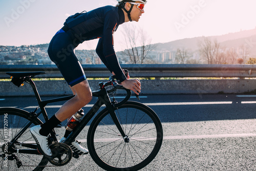 Young skinny climber cyclist races up a sunset lined road in spanish mountains