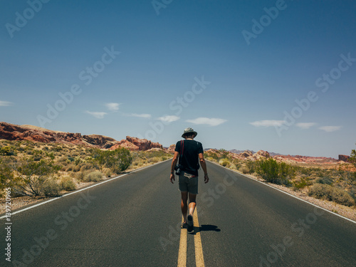 Fototapeta Naklejka Na Ścianę i Meble -  A handsome young tourist walking in the middle of the road on the hot summer day in valley of fire national park