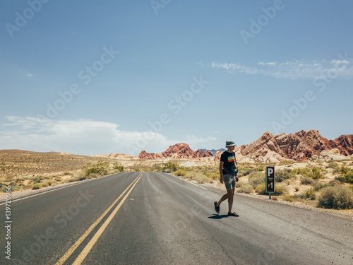 A young hipster tourist walking through the road in the desert in the valley of fire national park © onewithahalf