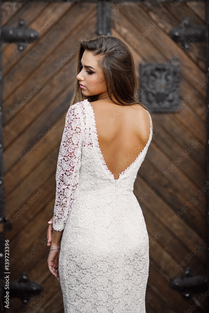 Gorgeous charming sexy bride in white lace dress with bare backs against the background of old wooden doors