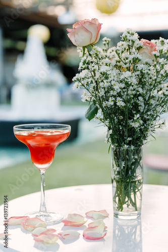 Red punch juice in a glass placed on a table decorated with flowers and daisies.