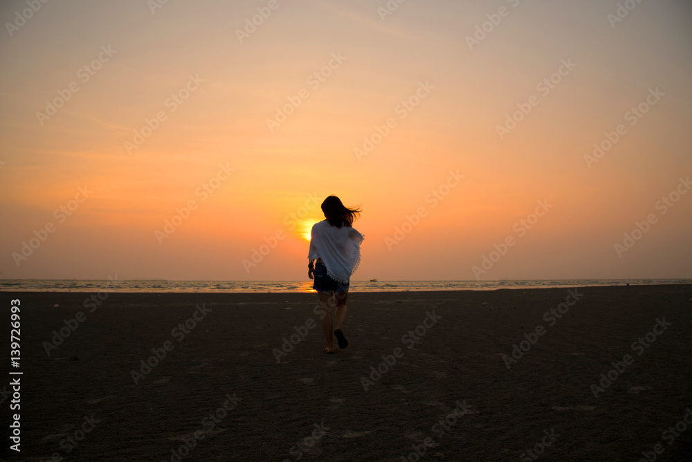 silhouette girl walk into the sea on sunset background