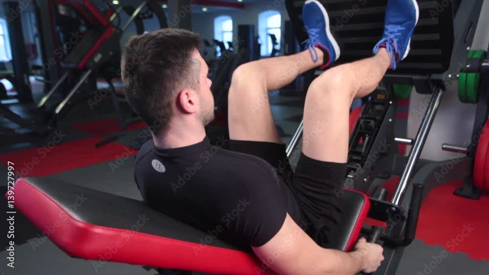 Man focused on training legs on the machine in the gym Man focused on training legs on the machine in the gym
