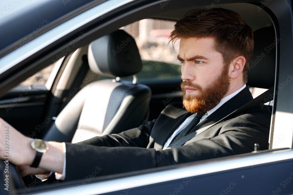 Portrait of a concentrated bearded man in suit driving car