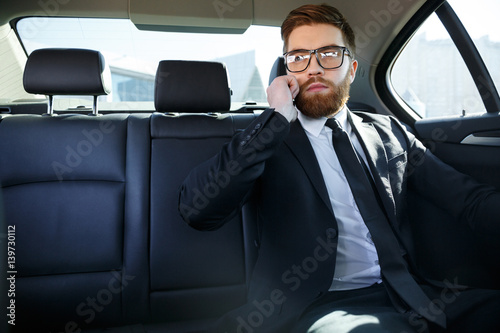 Young serious businessman sitting in car and talking on phone © Drobot Dean