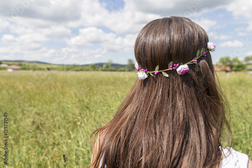 Beautiful young girl in summer field with grain and flower garland on hair