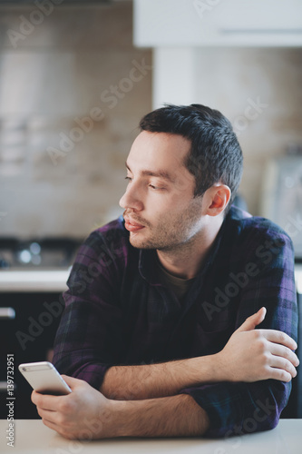Man is thinking on kitchen with smart phone in his hand