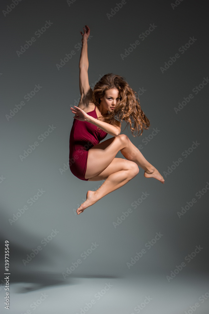 Fototapeta premium Beautiful woman dancer wearing maroon swimsuit posing on a grey studio background