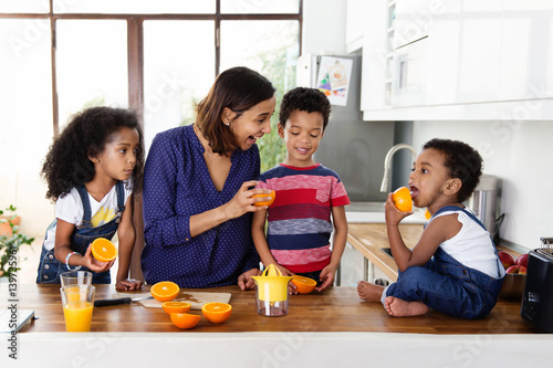 Une mère et ses trois enfants préparent du jus d'orange dans la cuisine photo