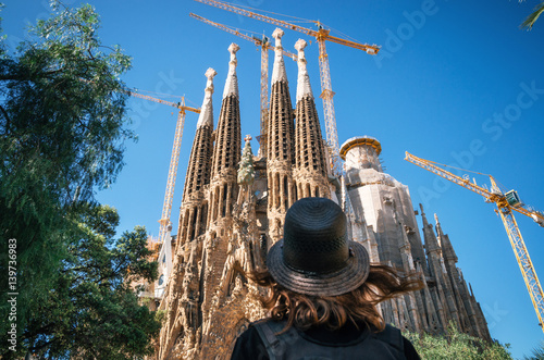 Young woman traveler in a hat looks at the Sagrada Familia the most famous tourist attraction of Barcelona, Catalonia Spain photo
