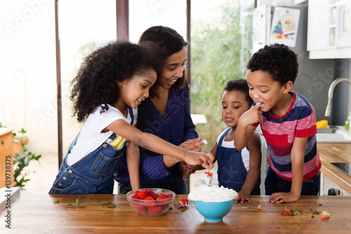 Une mère et ses enfants mangent des fraises avec de la chantilly dans la cuisine photo