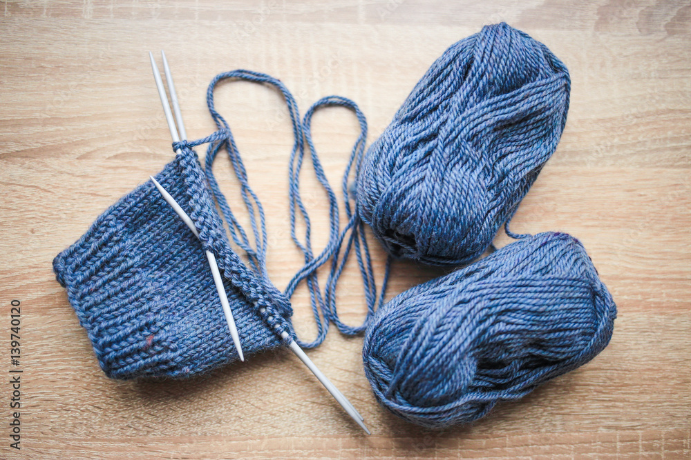 Knitting needles, loop counter and blue yarn are on the table. Wooden background. Hobbies 