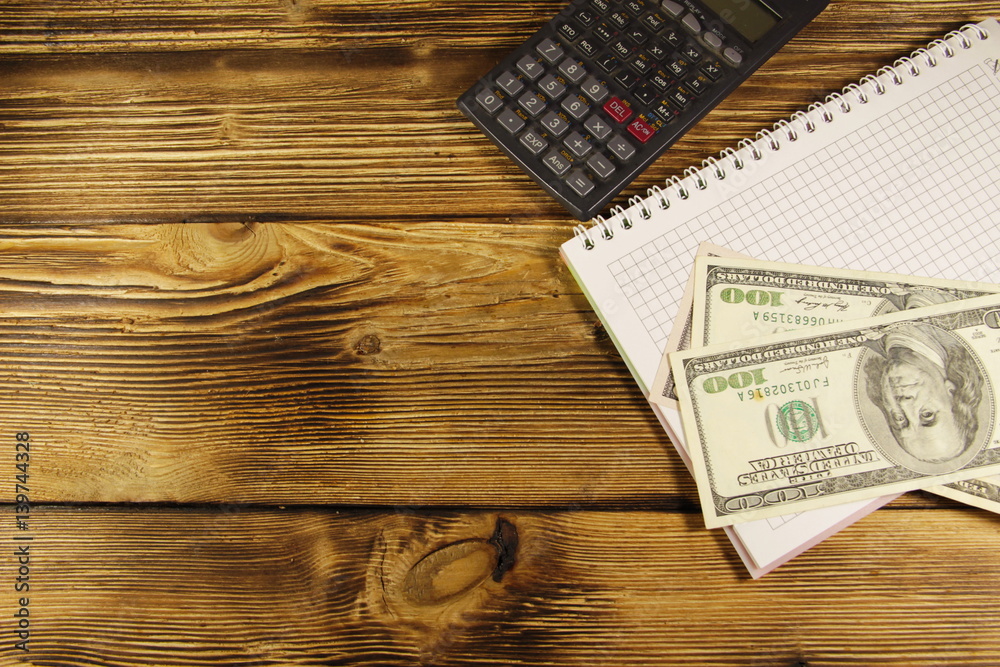 Notebook with dollars and calculator on wooden desk Notebook with dollars and calculator on wooden desk