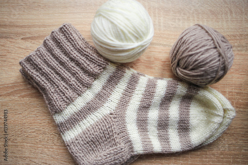 Beige and white yarn, beige-beige sock are on the table. Wooden background. Hobbies 