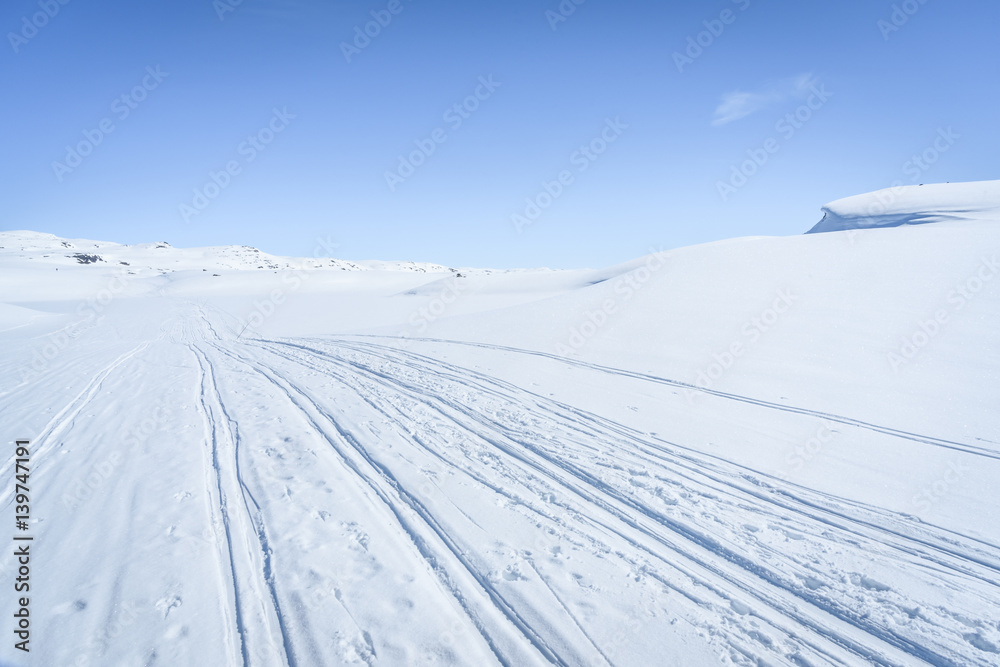 Clear sunny sky with skiing tracks in a winter landscape in snow covered mountains