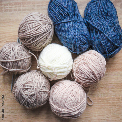 Knitting needles, beige, white and blue yarn are on the table. Wooden background. Hobbies 