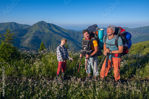 Happy travelers - men and boy stand on the alpine meadow among the lush wildflowers and enjoying life