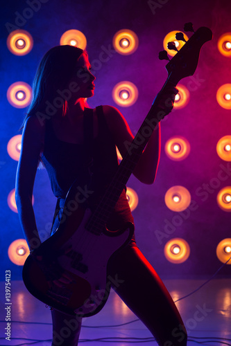 Silhouette girl with a guitar in hands on stage singing a song in rock style, close-up