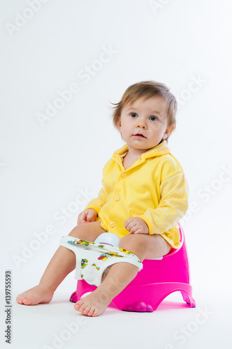 Little smiling girl sitting on a pot. Isolated on white background.
