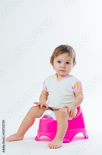 Little smiling girl sitting on a pot. Isolated on white background.