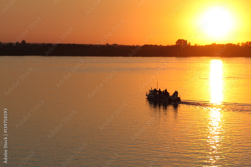 Naklejka premium Boat with people on a sunset background floating on the river