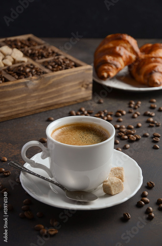 Cup of fresh coffee with croissants on dark background, selective focus