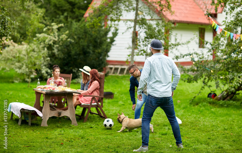 friends playing football with dog at summer garden photo