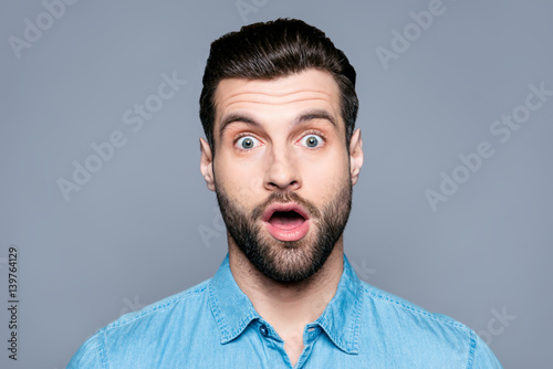A close up portrait of a young surprised man with opened mouth isolated on gray background