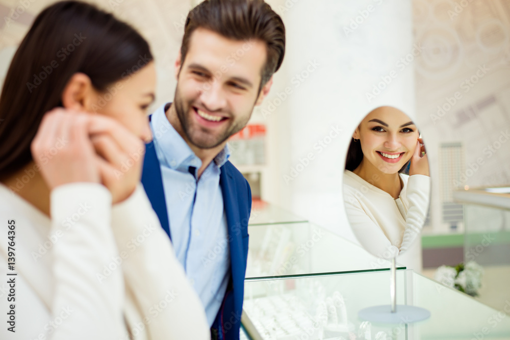 Happy beautiful young woman with her success boyfriend trying earring near mirror in jewelry store Happy beautiful young woman with her success boyfriend trying earring near mirror in jewelry store