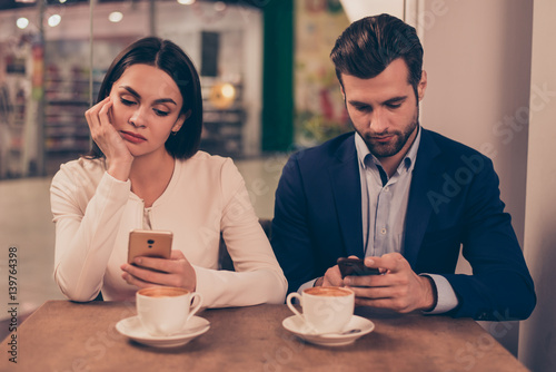 Bored couple sitting in a cafe holding phones