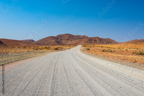 Gravel 4x4 road crossing the colorful desert at Twyfelfontein, in the majestic Damaraland Brandberg, scenic travel destination in Namibia, Africa.