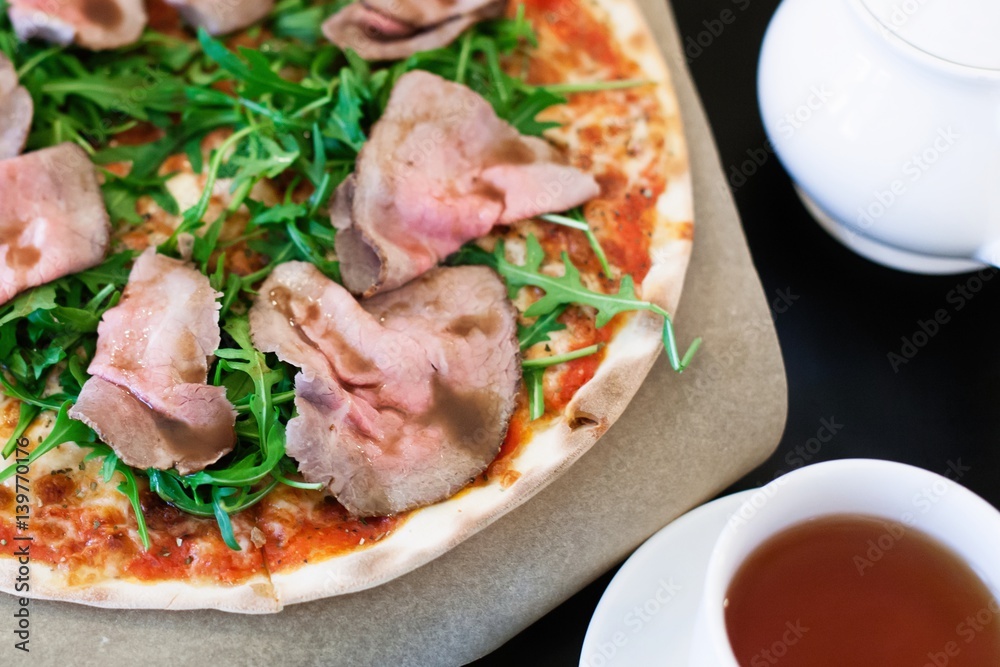 Pizza with roast beef and rocket salad on a table