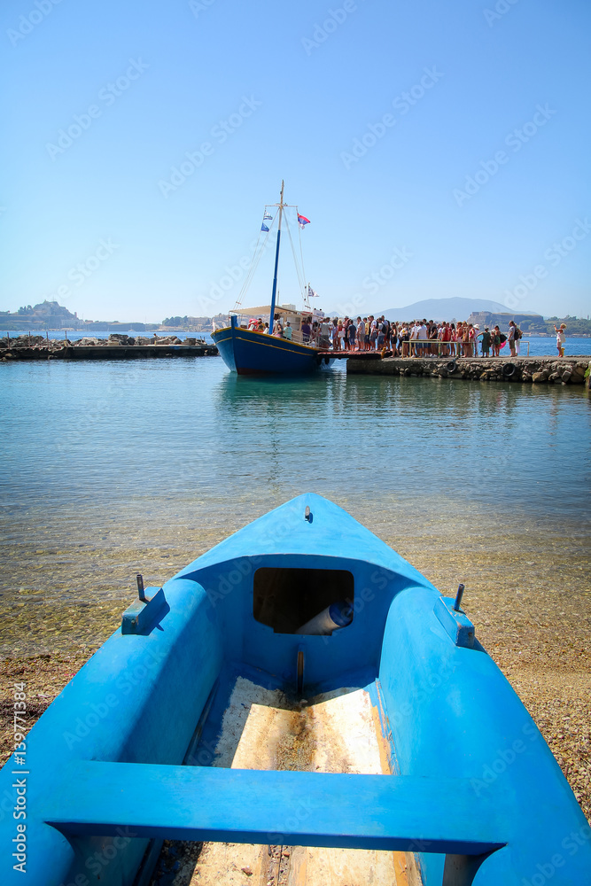 Blue fishing boat docked on the beach in front a yacht
