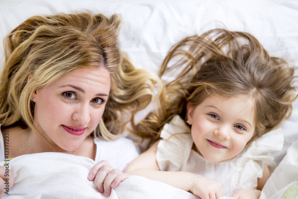 Cute little girl and her mother lying on a bed Cute little girl and her mother lying on a bed